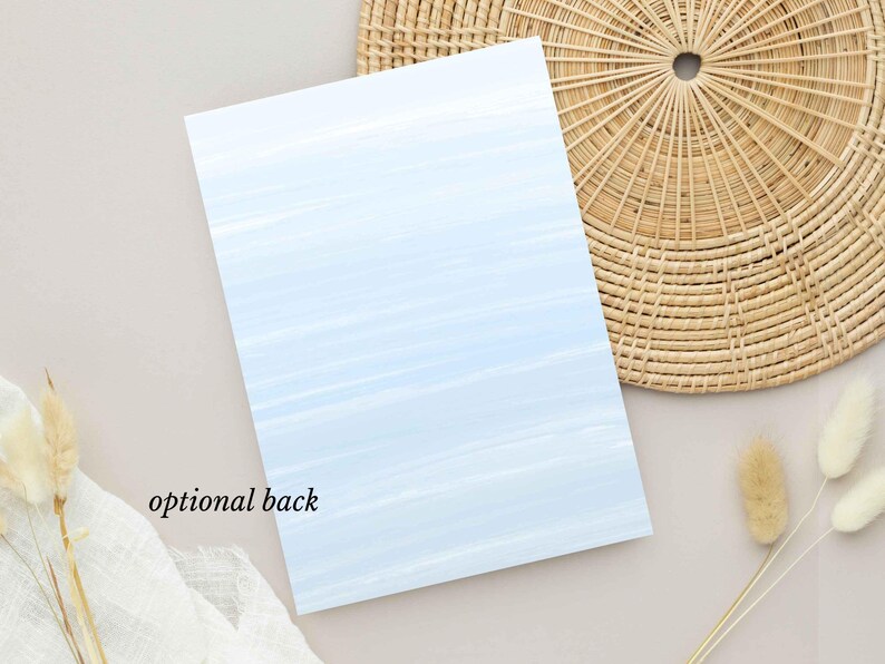 May include: A rectangular card with a light blue watercolor wash design. The text "optional back" is printed in black at the bottom left. The card is placed on a neutral surface with a woven placemat and dried floral accents.