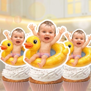 Könnte beinhalten: Drei Cupcakes mit einem Baby in einem gelben Enten-Schwimmring. Die Babys lächeln und heben die Arme. Die Cupcakes haben weißes Frosting und befinden sich in rosa Cupcake-Formen. Der Hintergrund ist unscharf.