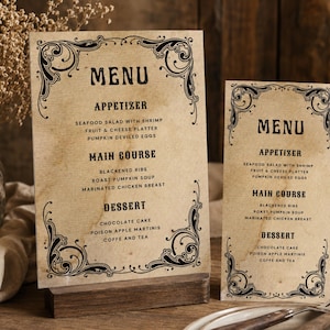 May include: Two rectangular menu cards with a light tan, aged paper texture and black ornate scrollwork borders. The text reads MENU, APPETIZER, MAIN COURSE, and DESSERT, followed by lists of food items including seafood salad, ribs, and chocolate cake.