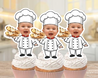 May include: Three cupcake toppers featuring a baby dressed as a chef, holding a plate of cannoli. The baby wears a white chef's hat and uniform with black buttons and a red collar. The cupcakes have white frosting and pink cupcake liners.