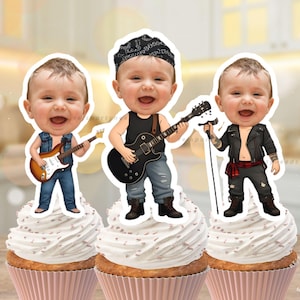 May include: Three cupcake toppers featuring cartoon babies dressed as rock stars. Each baby is on top of a cupcake with white frosting and a pink liner. One baby plays a guitar, one sings into a microphone, and one plays a black guitar.