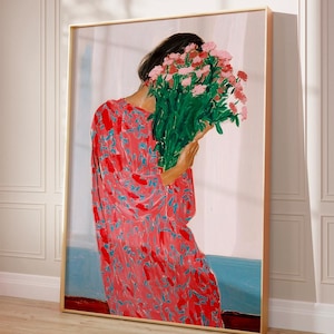 Peut inclure: Une impression d'art encadrée représente une personne tenant un grand bouquet de fleurs roses. La personne porte une robe rouge à motifs floraux bleus. L'arrière-plan présente un mur blanc avec une bande bleue.