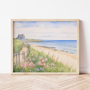 Peut inclure: Peinture à l'aquarelle d'une scène côtière. Une maison grise est située sur une colline herbeuse surplombant une plage de sable et un océan bleu. Une clôture et un sentier en bois mènent à la plage, avec des fleurs roses et violettes au premier plan. L'œuvre est encadrée en bois clair.