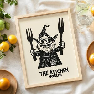 May include: A framed print featuring a whimsical illustration of a goblin holding two forks. The goblin is depicted in black and white with a long beard and pointed ears. The text "THE KITCHEN GOBLIN" is printed below the goblin.