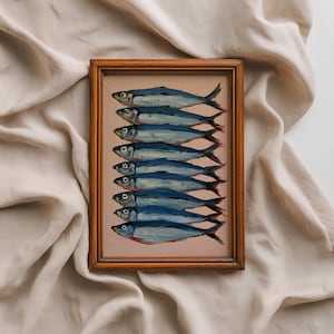 May include: A rectangular wooden frame containing an oil painting of eight stacked blue and silver fish arranged horizontally. The fish are depicted with visible brushstrokes in shades of navy, light blue, and white against a muted pink background.