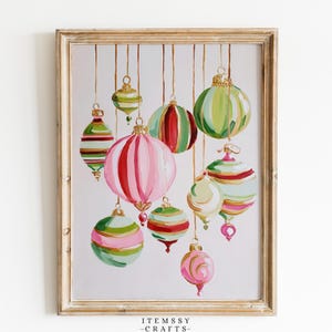 May include: A framed painting featuring various hanging Christmas ornaments in shades of pink, red, green, and gold. The ornaments have striped and solid patterns, suspended by thin gold lines. The text ITEMSSY CRAFTS is printed at the bottom.