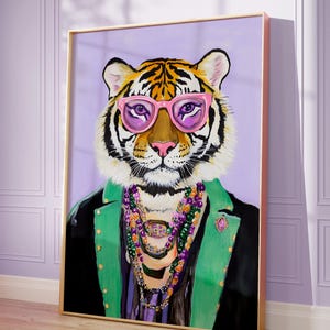 May include: A framed painting of a tiger wearing pink glasses, a green jacket, and a beaded necklace. The tiger is set against a purple background. The frame is gold.
