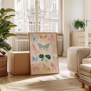 May include: A framed art print featuring watercolor butterflies in various colors, including blue, pink, and orange. The artwork is displayed in a bright, airy room with natural light, a large window, and a wooden floor.