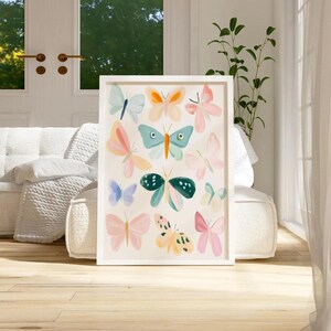 May include: A framed art print featuring a collection of colorful butterfly illustrations. The butterflies are depicted in various pastel shades, including pink, blue, and yellow, against a cream background. The artwork is encased in a white frame and displayed indoors.