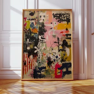 May include: Abstract art print in a gold frame. The artwork features a vibrant mix of colours, including pink, yellow, black, and red. The composition includes brushstrokes, splatters, and vertical red stripes, creating a dynamic and expressive piece.