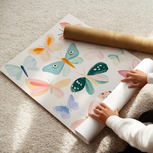 May include: A large sheet of paper with watercolor butterfly illustrations in pastel colors. The butterflies are in shades of blue, pink, orange, and green. A rolled-up paper tube is next to the sheet.