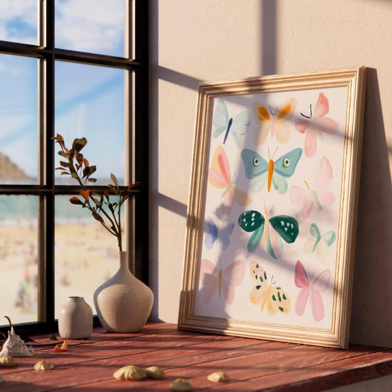 May include: A framed art print featuring colorful butterfly illustrations in shades of blue, pink, yellow, and green. The artwork is displayed on a wooden surface near a window, with a vase of dried branches and small decorative objects.