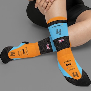 May include: A pair of orange, black, and light blue socks. The socks feature the McLaren logo, the number 4, and the Union Jack flag. The socks also have the Velo and Chrome logos.