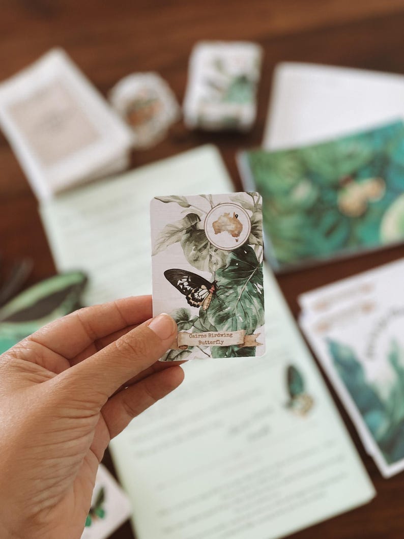 May include: A rectangular card featuring a black and white butterfly with the text "Cairns Birdwing Butterfly" on a banner. The card has a watercolor design of green leaves and a map of Australia. Other stationery items are in the background.