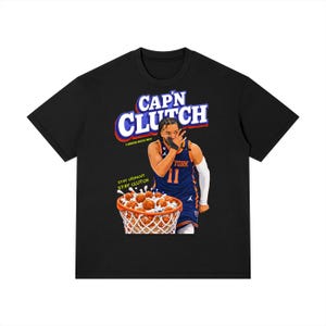 May include: Black t-shirt featuring a graphic of a basketball player with the text "CAP'N CLUTCH" in a cereal box style. The design includes a basketball net filled with cereal and the words "STAY CRUNCHY STAY CLUTCH".