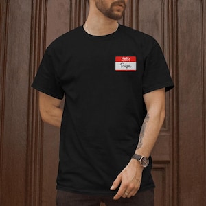 May include: Black t-shirt with a red and white name tag that says "Hello my name is Papi".