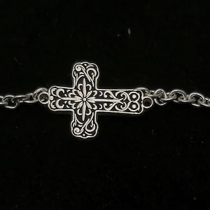 May include: A silver chain necklace with a detailed cross pendant. The cross has a floral design and a star in the center.