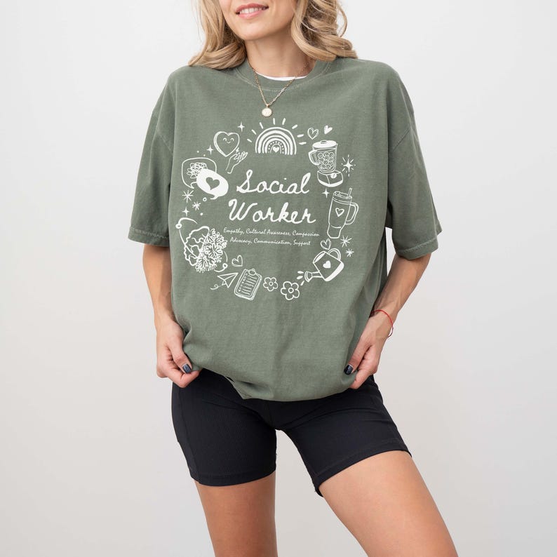 May include: A green t-shirt with a white graphic design that says "Social Worker" surrounded by illustrations of hearts, a sun, a coffee cup, a watering can, and other objects.