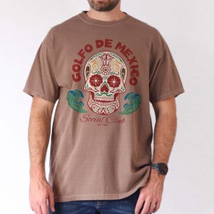 May include: A brown t-shirt with a colorful skull graphic and the text "Golfo de Mexico Social Club Est. 1930".
