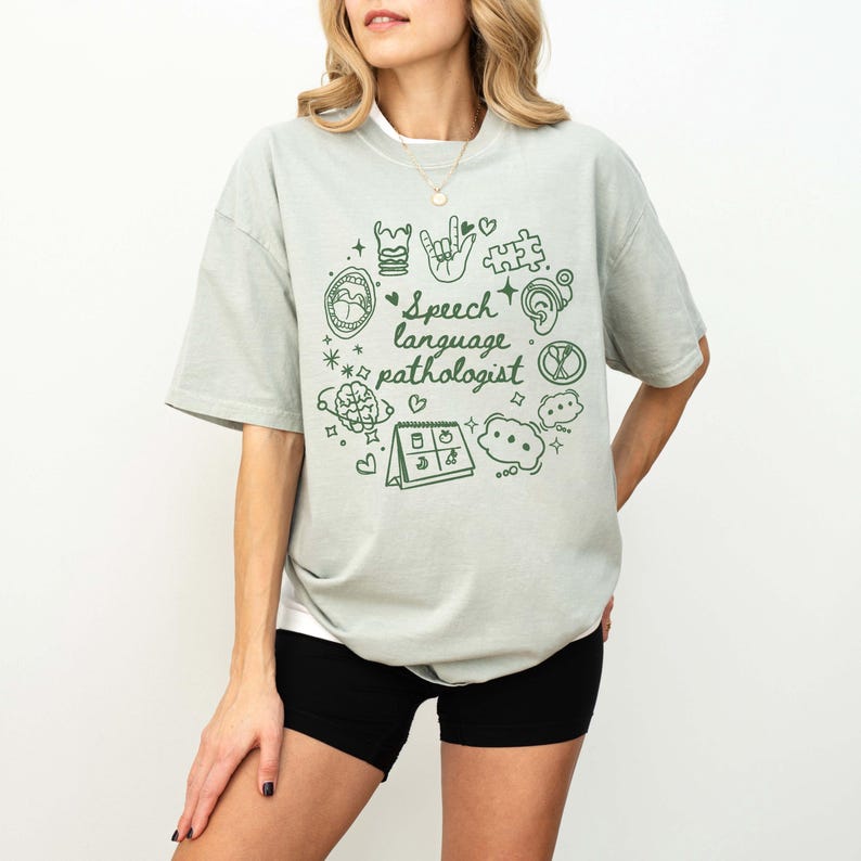 K&ouml;nnte beinhalten: Ein hellgr&uuml;nes T-Shirt mit einem grafischen Design von Logop&auml;die-Symbolen und dem Text "Speech language pathologist".