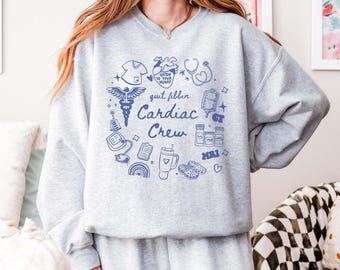 May include: Grey sweatshirt with a blue graphic print of medical symbols and the text "quit fibbin Cardiac Crew".