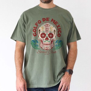 May include: A green t-shirt with a colorful sugar skull graphic and the text "Golfo de Mexico Social Club Est. 1930".