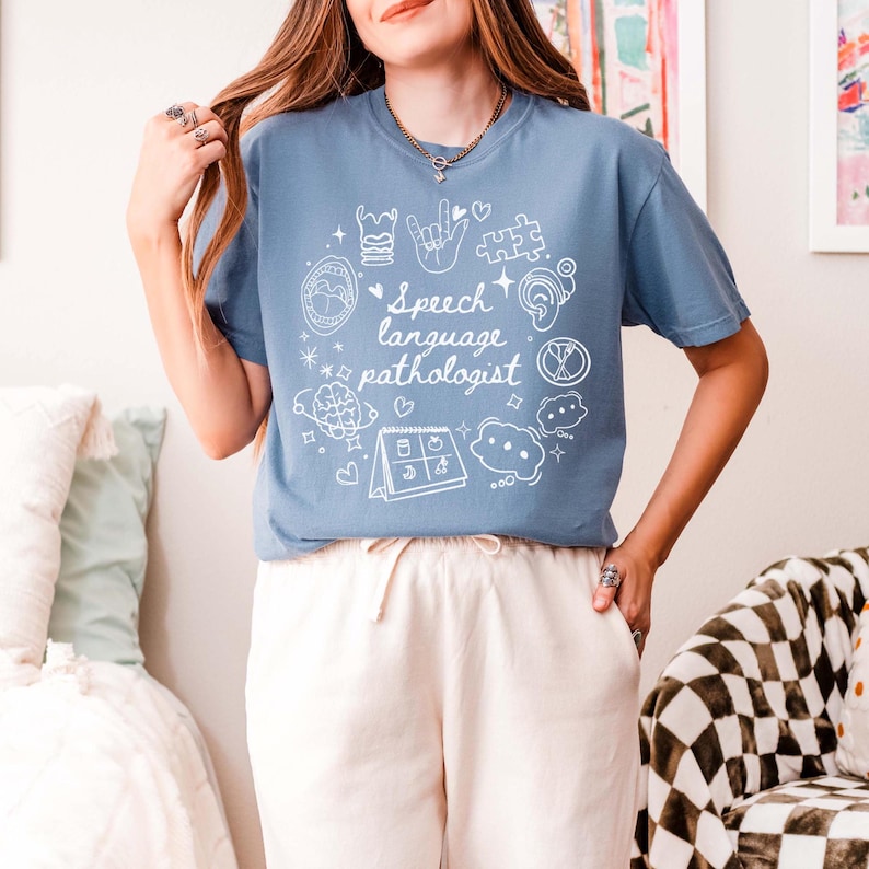 K&ouml;nnte beinhalten: Ein hellblaues T-Shirt mit einem wei&szlig;en Design aus Logop&auml;die-Symbolen und dem Text "Speech language pathologist".