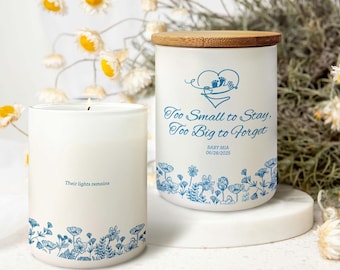 May include: Two white candles with blue floral designs and text. One candle reads "Their lights remains." The other candle has a wooden lid and reads "Too Small to Stay, Too Big to Forget" with a baby footprint design and the name "BABY MIA" and date.