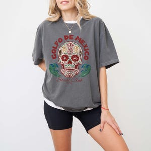 May include: Gray t-shirt with a colorful sugar skull graphic and the text "Golfo de Mexico Social Club Est. 1992".