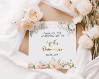 May include: A white invitation card with floral accents and the text "Thank you for celebrating with me" and "April's Quinceañera". The card is decorated with pink and white flowers and rests on a brown envelope.