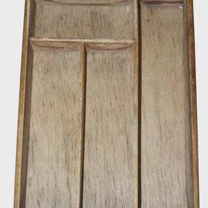 Puede incluir: Una bandeja rectangular de madera con acabado natural. La bandeja está dividida en cuatro compartimentos, con un recorte para el asa en la parte superior. La veta de la madera es visible en toda la bandeja.