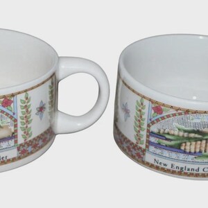May include: Two white ceramic soup mugs with handles. Each mug features a decorative band with an illustration of corn and the text "New England Corn Chowder". The mugs have a wide, shallow bowl shape.