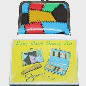 Op de afbeelding: Een kleurrijke Patty Patch Naaiset met een bijpassende portemonnee. De portemonnee heeft een patchwork ontwerp in rood, blauw, groen, geel en zwart. De set bevat een liniaal, schaar en veiligheidsspelden. De doos is geel met de tekst "Patty Patch Sewing Kit".