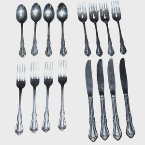 Puede incluir: Un conjunto de cubiertos de plata antiguos, que incluye cucharas, tenedores y cuchillos. La cubertería tiene mangos ornamentados y un acabado plateado. La disposición incluye cuatro cucharas, ocho tenedores y cuatro cuchillos, todo sobre un fondo blanco.