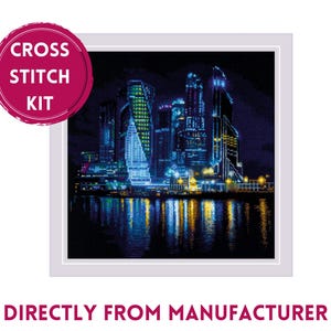 May include: Cross stitch kit featuring a nighttime cityscape with tall buildings reflected in the water. The buildings are lit up in blue, green, and yellow lights.