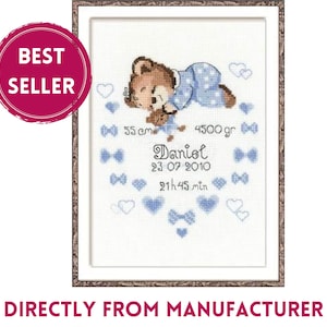 May include: Cross-stitch artwork in a wooden frame featuring a sleeping teddy bear wearing blue pajamas. The artwork includes the name "Daniel", birth date, time, and measurements: 55 cm and 4500 grams. The text "BEST SELLER" is in a pink circle.