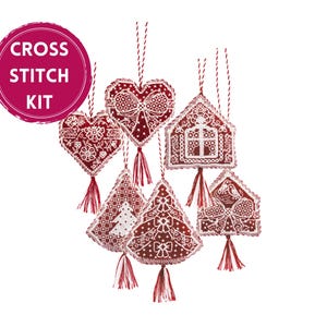 May include: A cross stitch kit featuring six hanging ornaments in deep red and white. The ornaments include heart, house, and tree shapes, each detailed with intricate white embroidery and finished with a matching red and white hanging tassel.