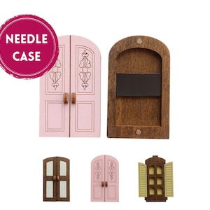 Könnte beinhalten: Eine Sammlung von Miniatur-Holztür- und Fensterdesigns. Das Set enthält eine rosa Doppeltür mit dekorativen Schnitzereien, eine braune Holzrückseite mit Magnet und andere Tür- und Fensterminiaturen. Der Text "NEEDLE CASE" befindet sich in einem rosa Kreis.