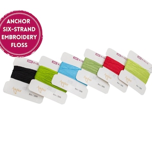 May include: A selection of Anchor six-strand embroidery floss in various colors, including black, green, blue, red, and yellow-green. Each spool is labeled with the brand name and color number. The text "Anchor Six-Strand Embroidery Floss" is in a pink circle.