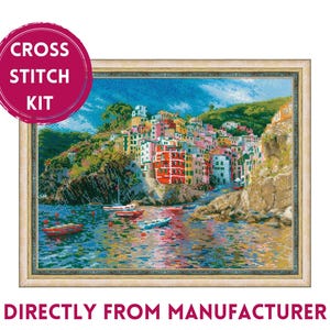 May include: Cross stitch kit featuring a colorful seaside town with buildings on a cliff overlooking a blue body of water with boats. The kit includes all the materials needed to complete the project.