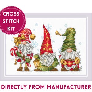 Könnte beinhalten: Kreuzstich-Set mit drei Gnomen, die rote, grüne und weiße Hüte tragen. Die Gnome halten einen Zuckerstock, eine Laterne und eine Tasse heiße Schokolade. Der Hintergrund ist weiß mit Schneeflocken.