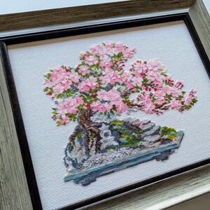The RIOLIS cross stitch kit Flowering Bonsai features a delicate bonsai design using 17 colors of wool/acrylic threads. The kit includes a needle, Zweigart 14ct white AIDA fabric, and a color chart. The finished size is 30x24 cm (11¾in x 9½in).