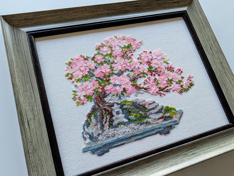 The RIOLIS cross stitch kit Flowering Bonsai features a delicate bonsai design using 17 colors of wool/acrylic threads. The kit includes a needle, Zweigart 14ct white AIDA fabric, and a color chart. The finished size is 30x24 cm (11¾in x 9½in).