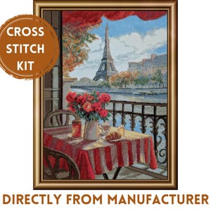 May include: A cross stitch kit featuring a framed scene of a balcony overlooking the Eiffel Tower in Paris. The image shows a table with a red and white striped tablecloth, a vase of red flowers, a croissant, and drinks, all set against a blue sky.