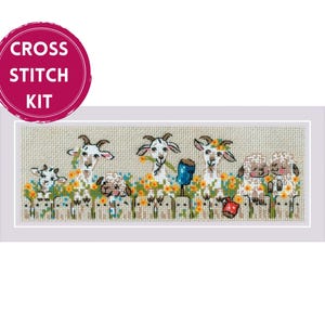May include: A cross stitch kit featuring a rectangular embroidery design of white goats and sheep standing behind a wooden fence amidst orange and yellow flowers. A pink circular badge in the top left corner displays the white text CROSS STITCH KIT.