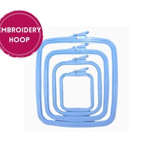Könnte beinhalten: Ein Stapel von vier hellblauen, quadratischen Stickrahmen in verschiedenen Größen. Jeder Rahmen hat einen Spannmechanismus. Das Bild enthält einen pinkfarbenen Kreis mit dem Text "EMBROIDERY HOOP".