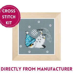 Puede incluir: Kit de punto de cruz con un diseño enmarcado de un muñeco de nieve blanco con gorro azul y patines, con copos de nieve sobre un fondo azul. El texto "CROSS STITCH KIT" está en un círculo rosa.