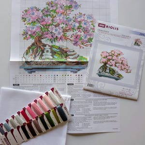 The RIOLIS cross stitch kit Flowering Bonsai features a delicate bonsai design using 17 colors of wool/acrylic threads. The kit includes a needle, Zweigart 14ct white AIDA fabric, and a color chart. The finished size is 30x24 cm (11¾in x 9½in).