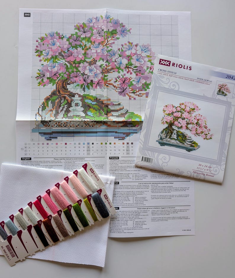 The RIOLIS cross stitch kit Flowering Bonsai features a delicate bonsai design using 17 colors of wool/acrylic threads. The kit includes a needle, Zweigart 14ct white AIDA fabric, and a color chart. The finished size is 30x24 cm (11¾in x 9½in).