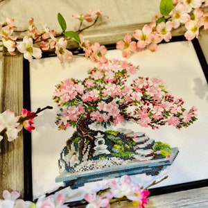 The RIOLIS cross stitch kit Flowering Bonsai features a delicate bonsai design using 17 colors of wool/acrylic threads. The kit includes a needle, Zweigart 14ct white AIDA fabric, and a color chart. The finished size is 30x24 cm (11¾in x 9½in).